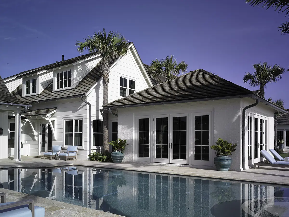 Exterior rear view of house with pool, deck, palm trees, and large windows.