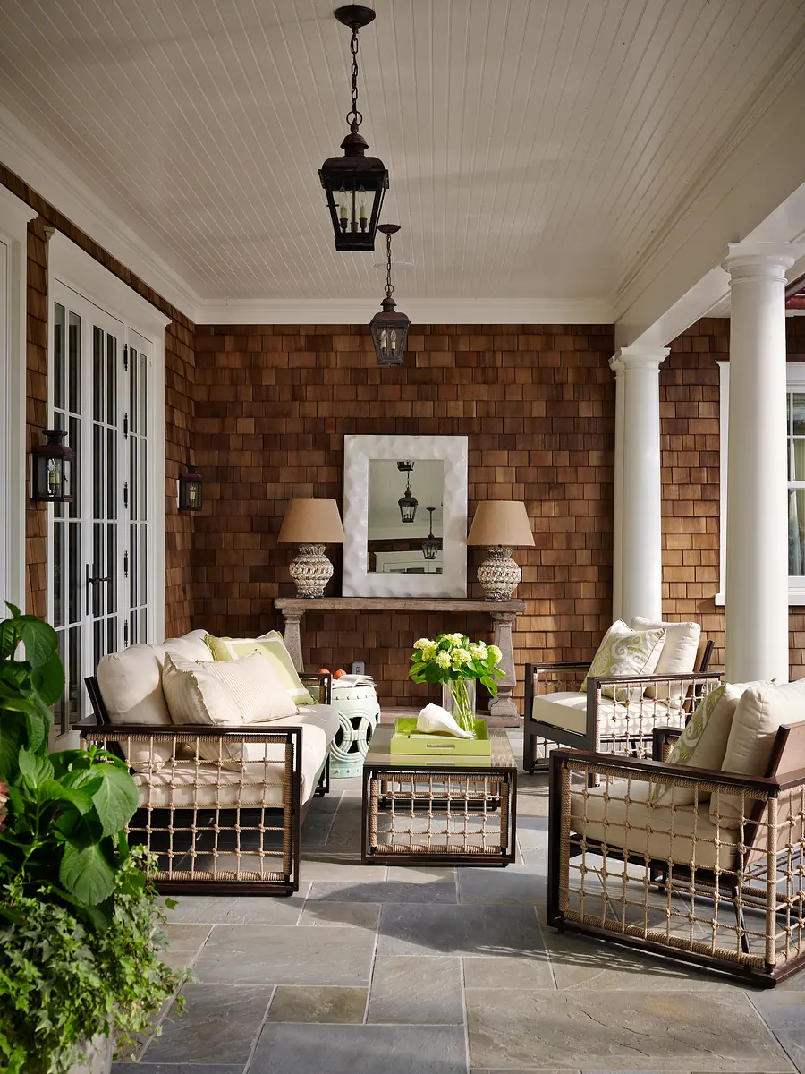 Patio with upholstered chairs, coffee table, potted flowers, wood shingle walls, and stone tile flooring.