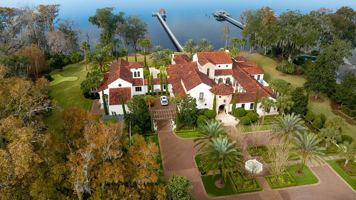 Front exterior view of a house with red-tiled roof, white walls, landscape, palm trees, and a fountain.