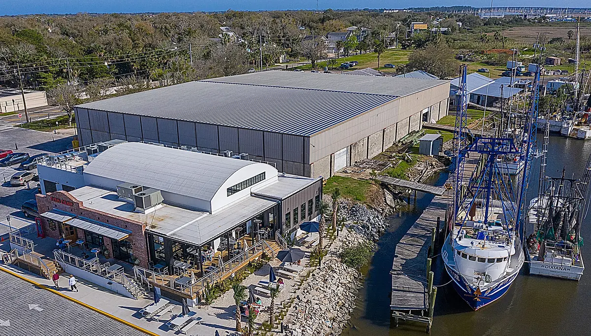 Exterior view of an industrial building and smaller brick structure with outdoor seating and docked boat.
