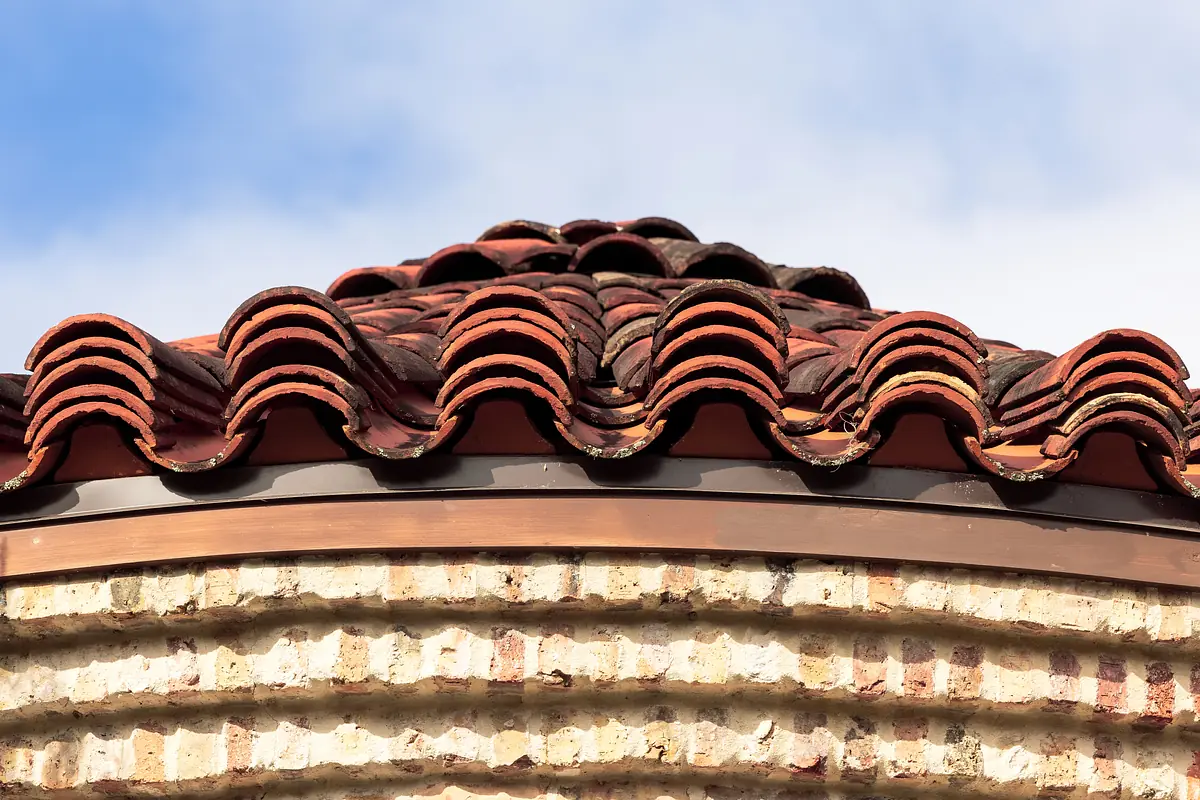 Close-up of terracotta roof tiles on circular brick structure with metal edging.