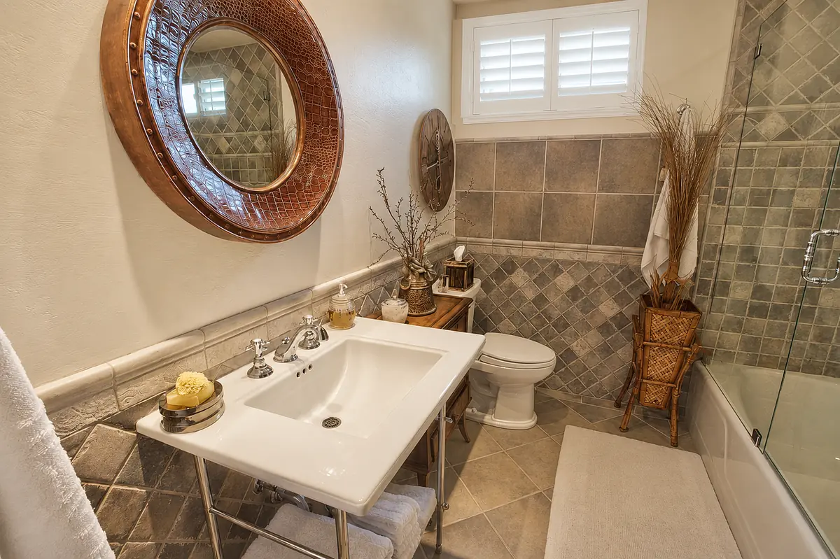 Bathroom with white sink, toilet, bathtub, round mirror, and patterned tile walls.