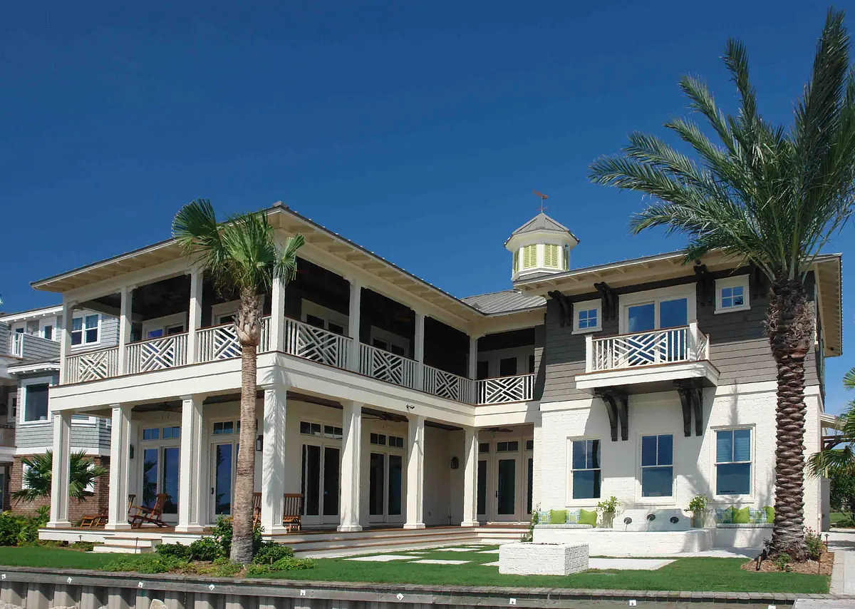 Exterior front view of a multi-story house with white and gray siding, porch, and palm trees.