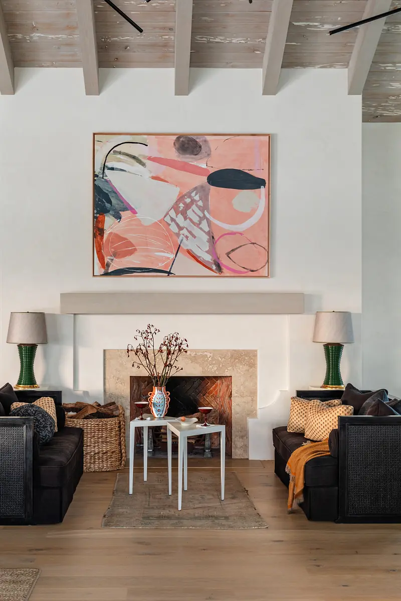 Living room with dark sofas, white coffee table, area rug, stone fireplace, and decorative artwork.