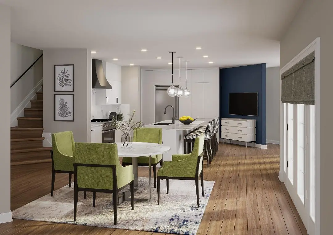 Dining room with round table, green chairs, rug, and connected kitchen area with white cabinetry and TV.