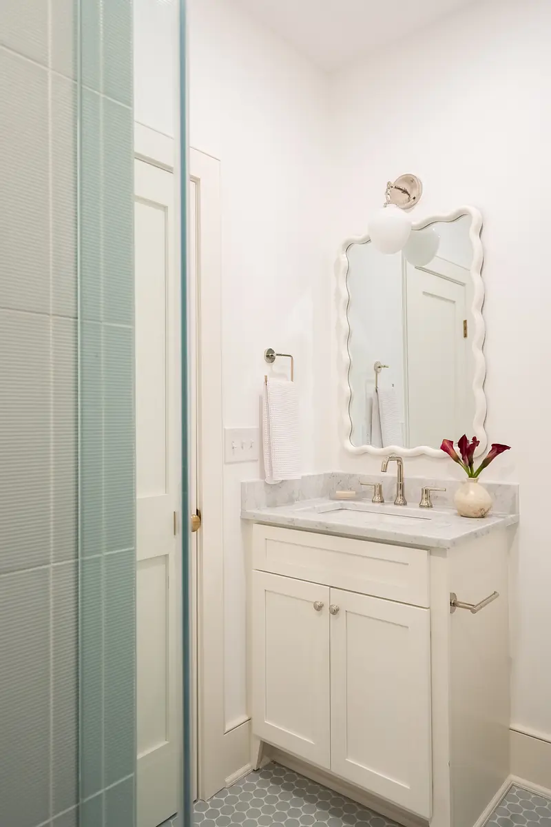 Bathroom with white vanity, marble countertop, round mirror, hexagonal tile floor, and glass shower enclosure