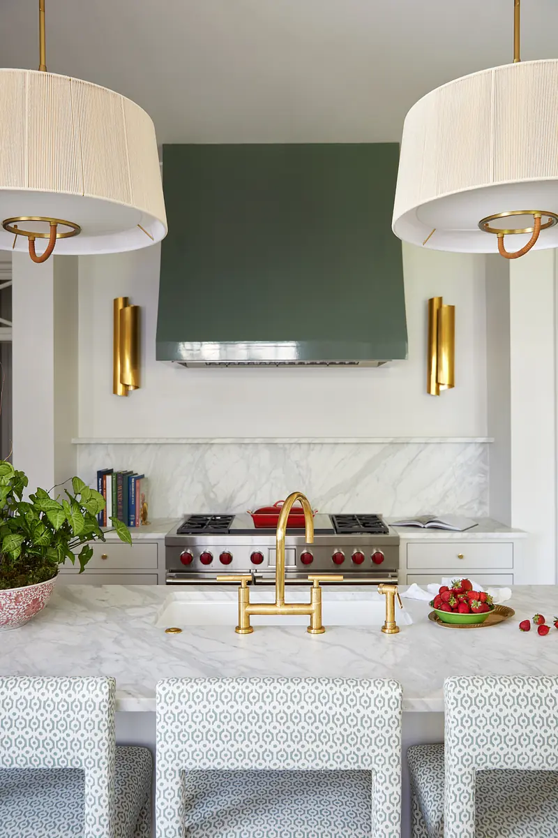 Kitchen with marble countertop, gold faucet, stove with red knobs, pendant lights, and decorative bowl of strawberries