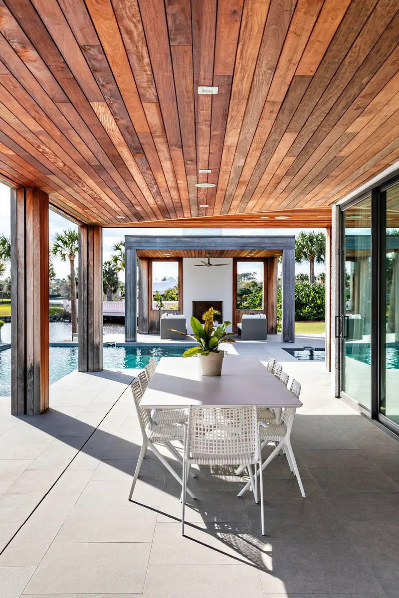Patio with white dining table, wicker chairs, wooden beams, pool view, and large gray tiled floor.