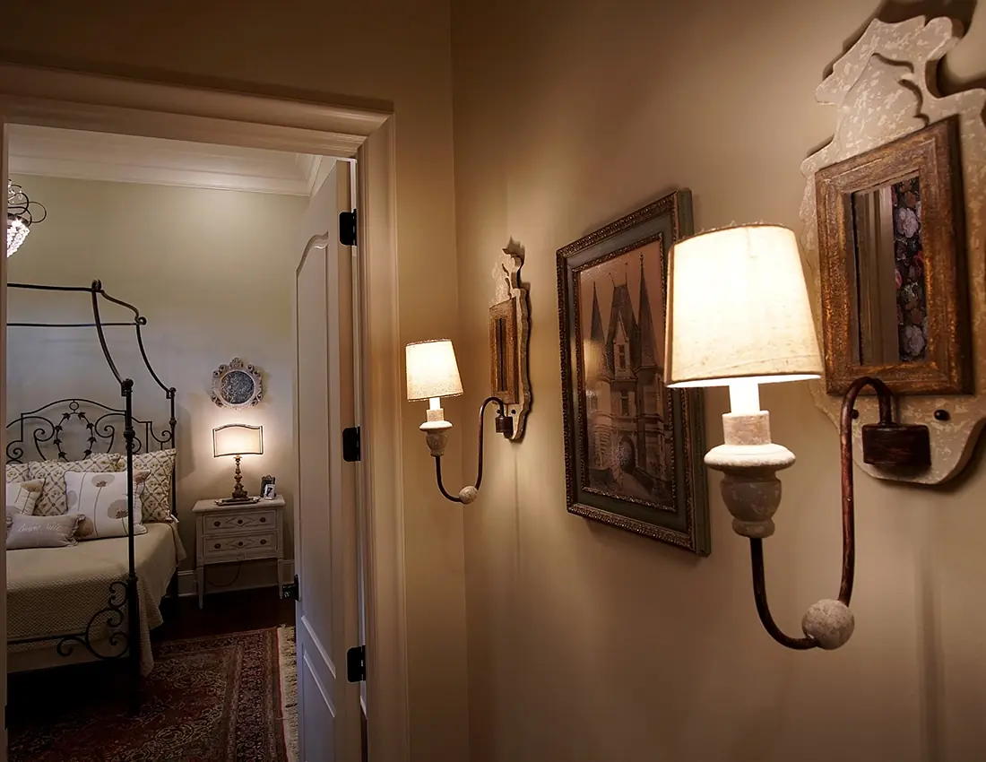 Hallway with wall sconces, framed artwork, and a red area rug leading to a bedroom.