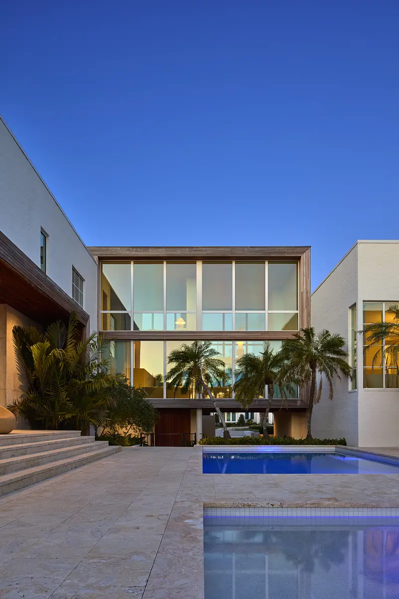 Exterior rear view of a house with large windows, palm trees, swimming pool, and stone steps.