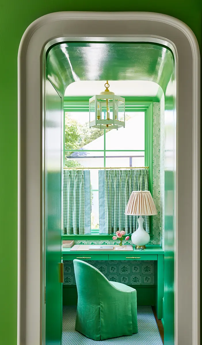 Small study area with green walls, green desk, matching chair, and window with patterned curtains.