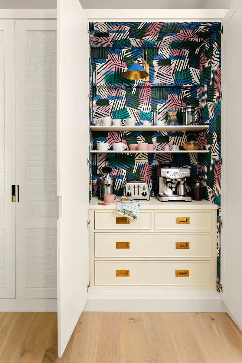 Closet with colorful leaf wallpaper, coffee machine, toaster, and storage drawers in white cabinetry