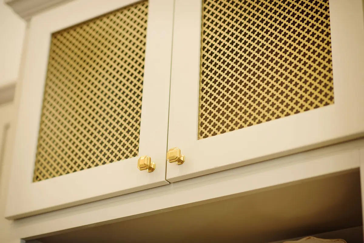 Upper cabinets with light frame and gold mesh doors, part of built-in structure on neutral backdrop.